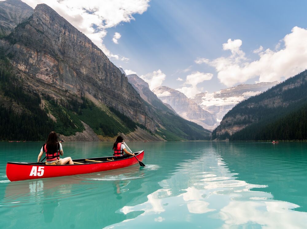 Two friends paddle in a canoe in an open lake surrounded by mountains in Lake Louise.